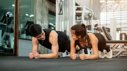 A sporty Asian male and female are performing a plank workout on the gym floor, training together.