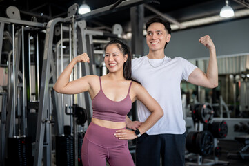 Fototapeta premium Two sporty and cheerful Asians, a male and female in sportswear, are standing in a professional gym.