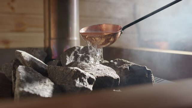 Steam rise from heated rocks as copper sauna ladle pours water on, closeup slomo