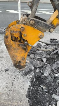 Close up view of excavator bucket digging the road surface.