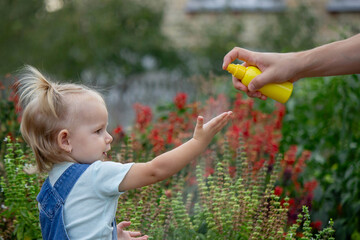 mother applies an aerosol insect spray to the child's body. Selective focus