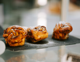 Freshly baked cinnamon rolls displayed on a black tray in a cozy bakery setting during the morning rush