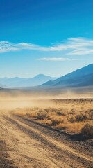Fototapeta premium Dusty Desert Road Leading Into Serene Mountains Under Clear Sky