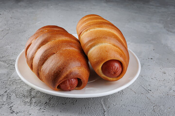 Two sausages in dough in a white plate on concrete.
