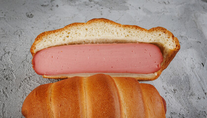 A cut and whole sausage in dough lie on concrete.