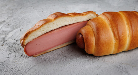 A cut and whole sausage in dough lie on concrete.