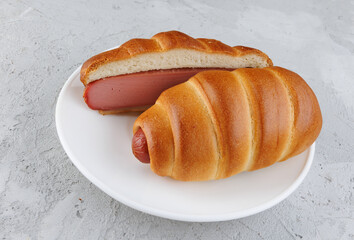 Sliced and whole sausages in dough in a white plate on concrete.