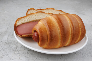 Sliced and whole sausages in dough in a white plate on concrete.