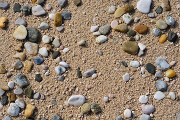 Close-up of a sandy beach reveals a pattern of pebbles scattered across the textured sand, creating a beautiful natural mosaic