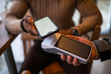Close up of  man makes a contactless payment with smartphone in the bar.