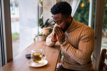 Young man sitting in bar, relaxing and drinking tea. He is blowing nose.