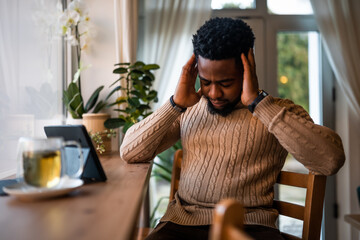 Freelancer using digital tablet to communicate online. He is sitting in bar and having video call. He has headache.