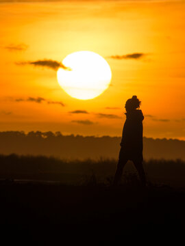 Fototapeta Femme seule photographiée au téléobjectif devant un coucher de soleil