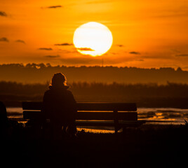Obraz premium Femme seule assise sur un banc photographiée au téléobjectif devant un coucher de soleil