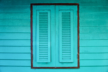 Green wooden window with shutters on a blue wooden wall. Vintage style.