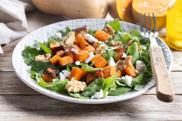 Pumpkin salad with arugula, walnuts and feta cheese on wooden
