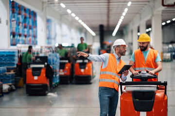 Warehouse workers discussing and driving pallet truck in large distribution center