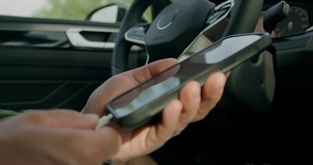 A man connects a mobile phone with a cable to a car while sitting in the driver's seat. Close-up of...