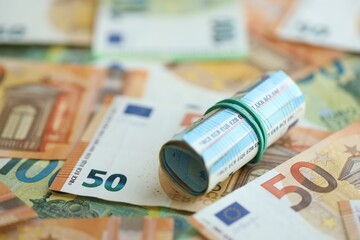 Roll of twenty euro currency bills lies on big amount of hundred and fifty euro banknotes