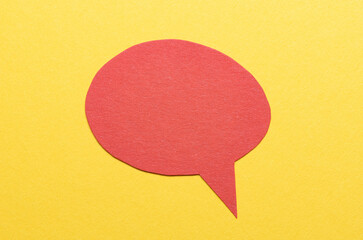 Red cut out blank paper speech bubble of round shape with copy space for text on yellow background, flat lay top view conceptual backdrop