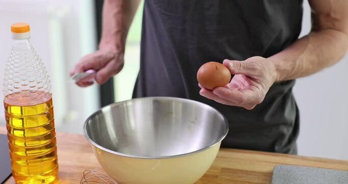 Professional chef cracks eggshell with sharp knife. Experienced cook prepares ingredients for cooking delicious pancakes in kitchen. Slow motion