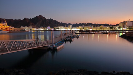 Naklejka premium The Muttrah corniche viewed from the jetty next to the fish market during the blue hour, with the mosque and mountains in the background, Muttrah, Muscat, Oman