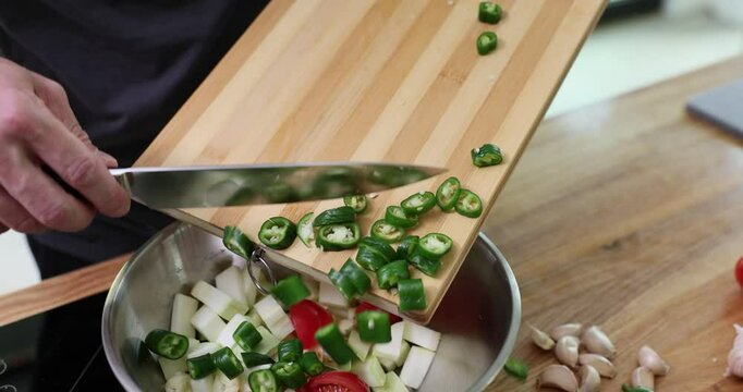Man chef adds chopped chili pepper into stainless steel bowl. Experienced cook prepares nutritious and delicious fresh salad. Slow motion