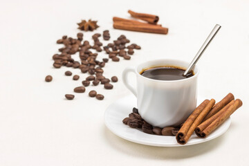 Cinnamon sticks and coffee grains on white saucer. Coffee drink in white cup.