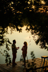 Senior couple talking on wooden pier by lake at sunset