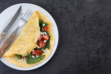 Stuffed omelette with tomatoes and spinach on black slate background. Top view. Copy space