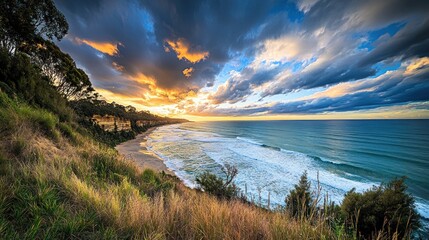 Obraz premium Dramatic sunrise over ocean beach, coastal cliffs, and grassy hills.