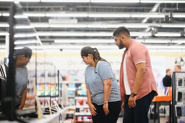 Beautiful couple buying consumer tech products in modern home appliances store. They are choosing home theater and TV devices