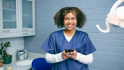Confident Female Healthcare Professional in Scrubs Smiling With Mobile Phone in a Modern Clinic...