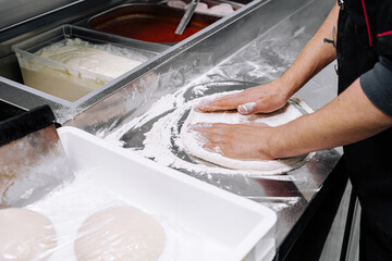Professional baker preparing dough in a well-equipped kitchen during a busy day of making fresh pizzas