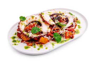 Tentacles of grilled octopus served with roasted vegetables and herbs on a white plate