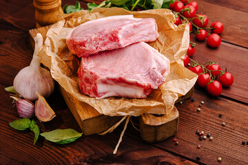 Fresh pork chops arranged on a wooden board with herbs and cherry tomatoes in a rustic kitchen setting