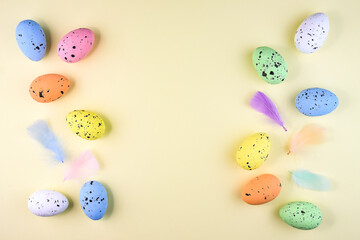 Colorful motley Easter eggs located along the edges of the image on a pastel yellow background with soft decorative feathers.