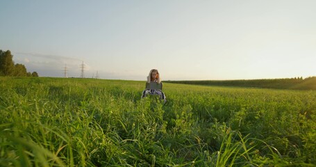 A red-haired woman poses sitting on a chair in the middle of a field, she looks at the camera. The light of the setting sun reflects off her hair