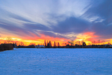 Fototapeta premium Colourful sunrise with glowing red clouds on a winter's day over the meadows and forests of Siebenbrunn, the smallest district of the Fugger city of Augsburg