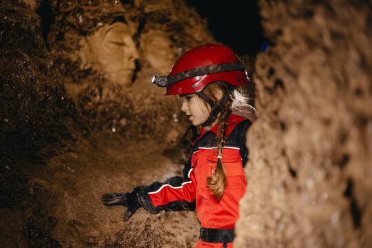 A 6-year-old girl in a protective suit and helmet with a flashlight in the middle of a natural underground cave is walking the tourist route of a caver