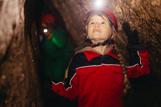 A little schoolgirl in a caving suit in a cramped dark cave enthusiastically follows the tourist route of a gypsum cave explorer