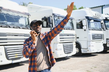 An African-American trucker is standing next to a truck and using a walkie-talkie
