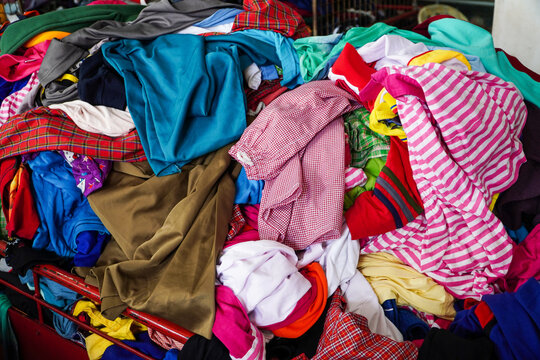 A large pile of various used clothing items in a cart. Different colors and patterns. A Mountain of Colorful Used Clothing for sell.