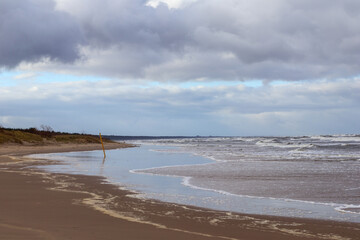 
a landscape with a sea and a beach with sand and water and a cloudy sky in the background.