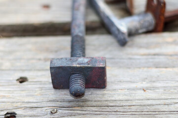 
a metal screw with a square head screwed into a wooden surface, with another metal object visible in the background.