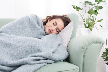 smiling serene woman sleeping on cozy sofa under warm soft plaid blanket in living room. Healthy...
