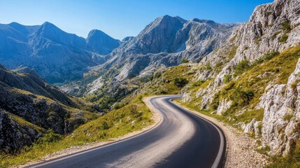 Fototapeta premium 75.A winding asphalt road cutting through a mountainous region, with rocky hills and steep cliffs on either side. The road is smooth and well-maintained, stretching ahead in a series of curves that