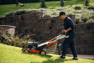 View from the side, cutting grass by lawn mover. Professional gardener is on the lawn