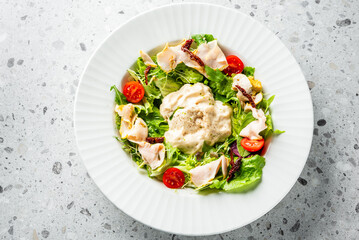 A fresh salad featuring lettuce, cherry tomatoes, sun-dried tomatoes, and sliced chicken, topped with a creamy dressing. Served in a white dish on a textured surface. Ideal for healthy food promotions