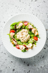 A fresh salad featuring lettuce, cherry tomatoes, sun-dried tomatoes, and sliced chicken, topped with a creamy dressing. Served in a white dish on a textured surface. Ideal for healthy food promotions